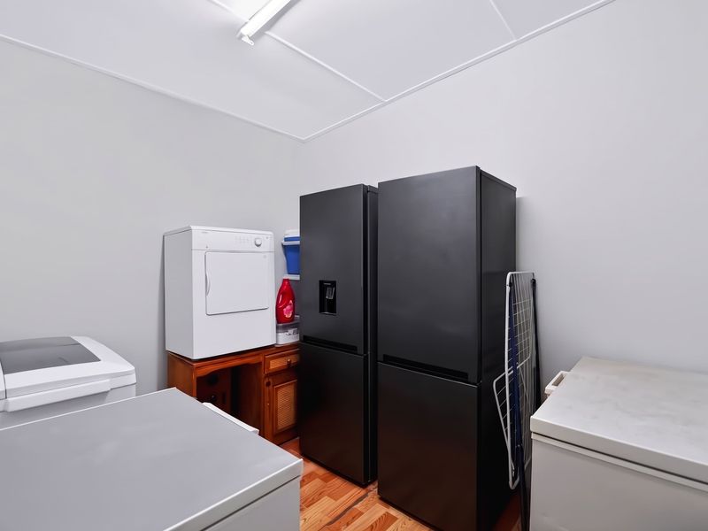 A functional laundry room featuring timber flooring and overhead lighting, currently utilized for appliance storage.