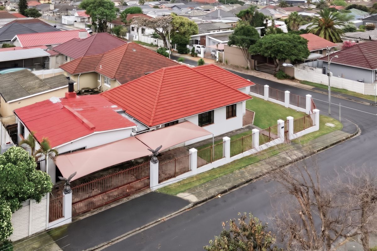 Aerial view of a residential property featuring a red tiled roof, perimeter wall with metal fencing, and a covered outdoor shade area.