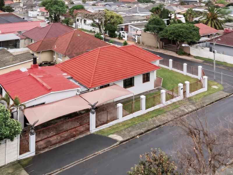 Aerial view of a residential property featuring a red tiled roof, perimeter wall with metal fencing, and a covered outdoor shade area.
