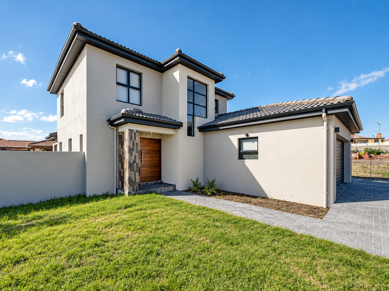 Modern double-storey townhouse exterior featuring a paved driveway, stone-clad entrance pillar, timber front door, and a well-maintained lawn.