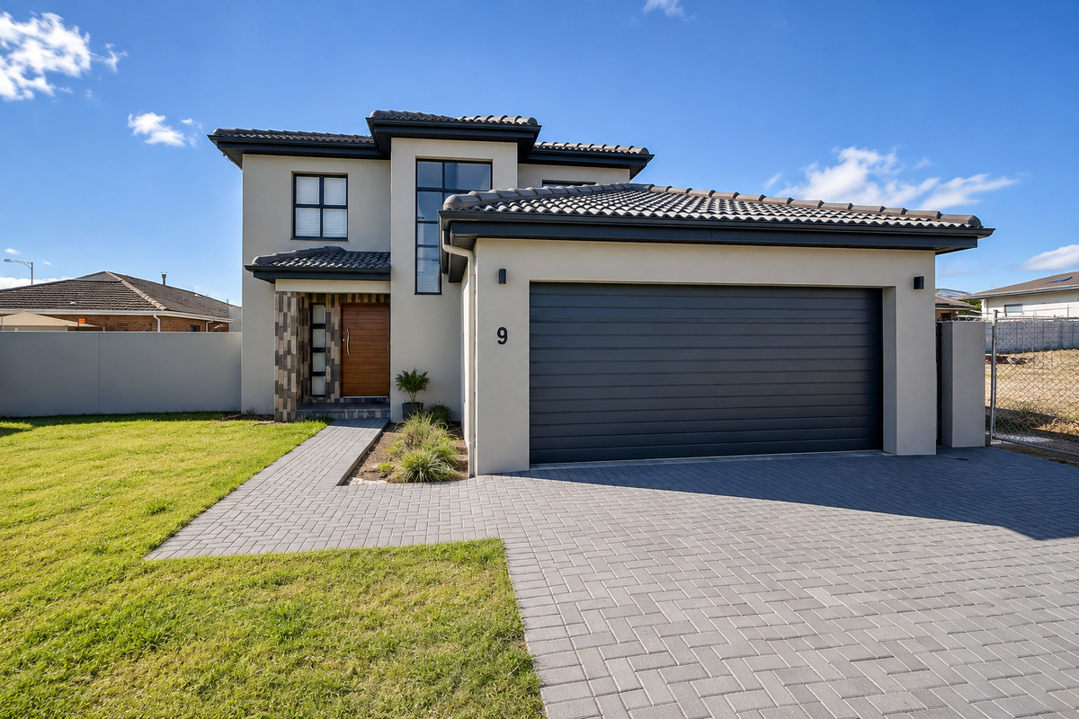 Modern double-storey townhouse featuring a sleek dark garage door, stone cladding accents, tiled roof, and a neat paved driveway with landscaped front lawn.