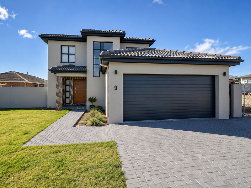 Modern double-storey townhouse featuring a sleek dark garage door, stone cladding accents, tiled roof, and a neat paved driveway with landscaped front lawn.