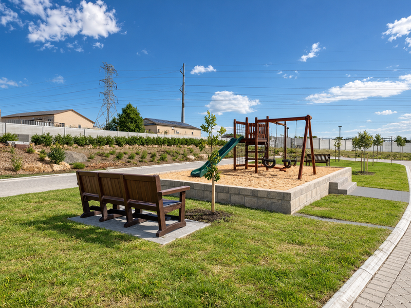 A well-maintained communal garden area featuring a sand pit, playground equipment, paved walkways, and landscaped green space within the residential estate.