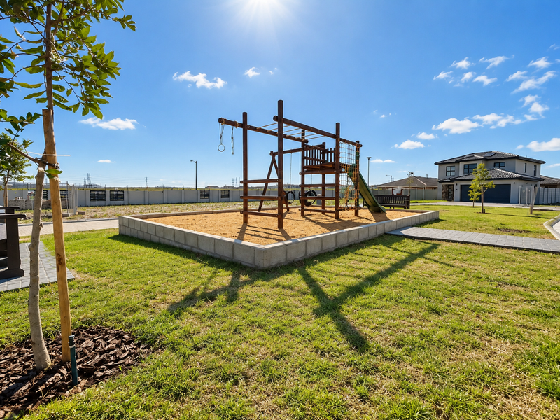 A well-maintained communal garden area featuring a sandpit, playground equipment, and paved walkways within a secure residential estate.