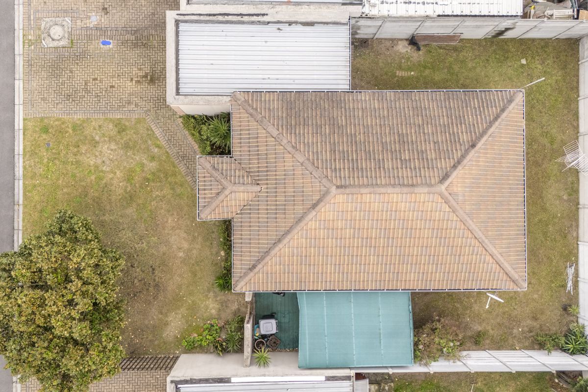 Aerial view of the property showing the tiled roof, surrounding garden, paved driveway, and boundary walling.