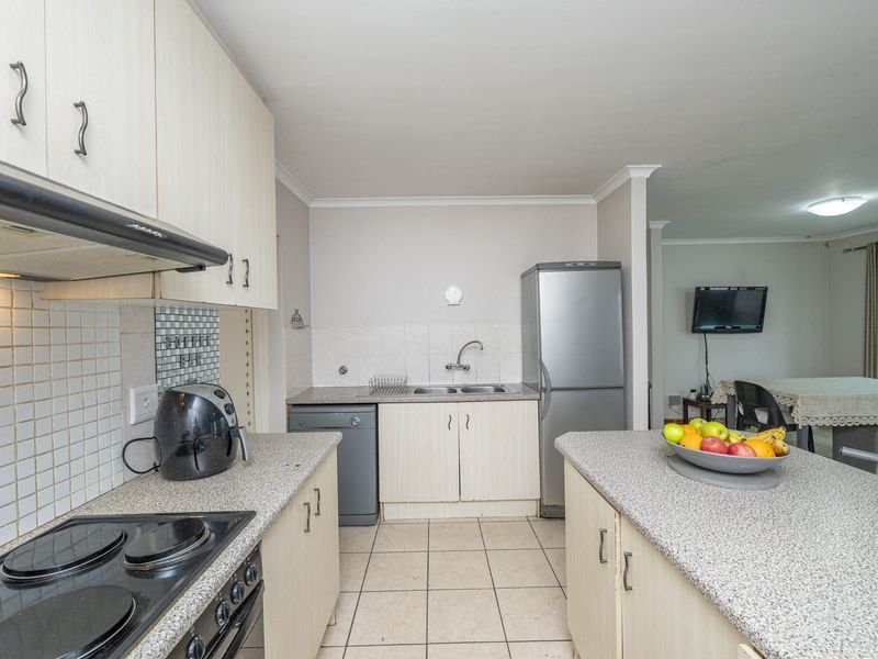 Open-plan kitchen featuring light-toned cabinetry, laminate countertops, built-in electric hob and oven, and tiled flooring, flowing into the adjacent living and dining area.