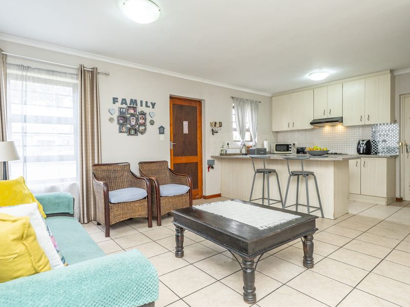 Open-plan living and kitchen area featuring tiled flooring, neutral cabinetry, granite countertops, and a breakfast bar, creating a functional and connected living space.