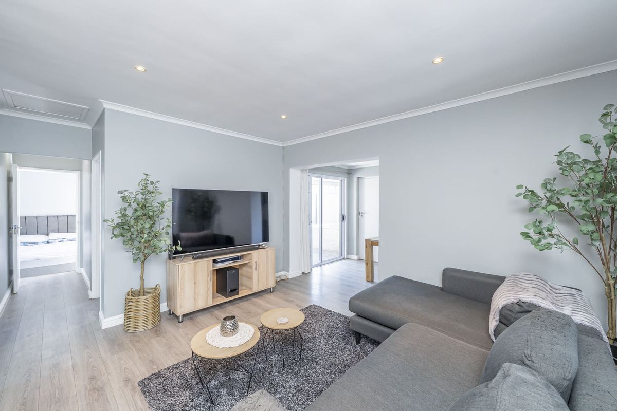 A bright and modern living room featuring light laminate flooring, recessed downlighting, and a sliding glass door providing access to the rear of the property.
