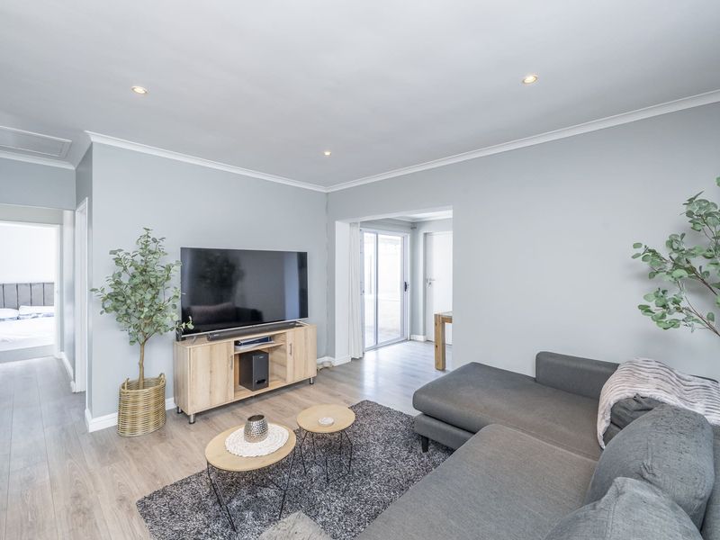 A bright and modern living room featuring light laminate flooring, recessed downlighting, and a sliding glass door providing access to the rear of the property.