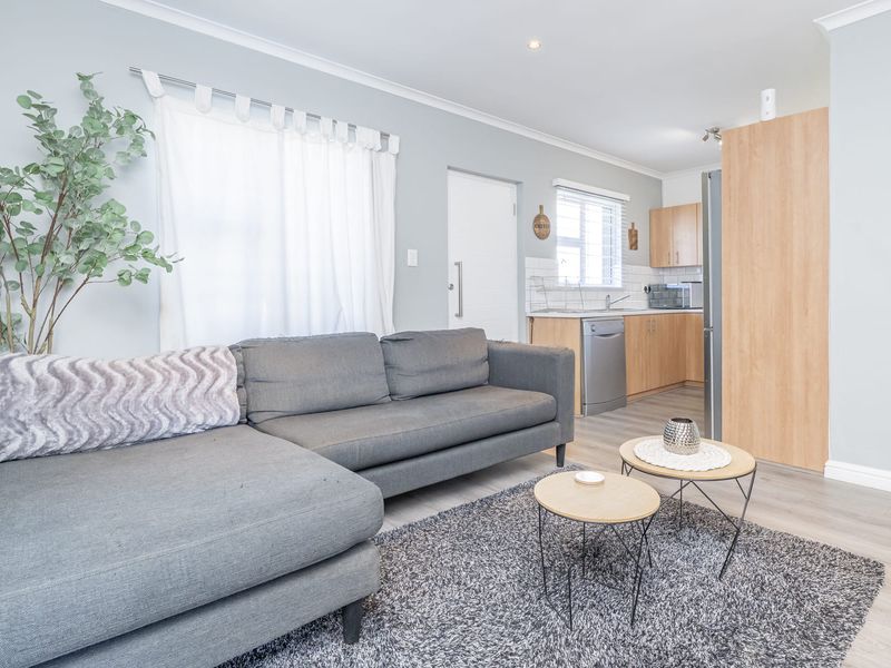 An open-plan living area featuring light laminate flooring, neutral walls, and a functional kitchen with built-in cabinetry and a tiled backsplash.