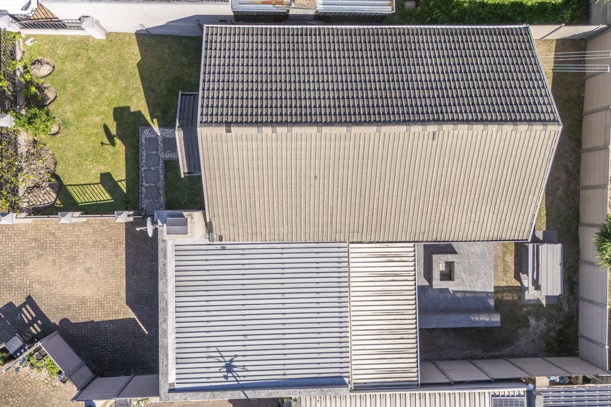 Aerial view of the property showing the roof structure, paved driveway, and surrounding garden area.