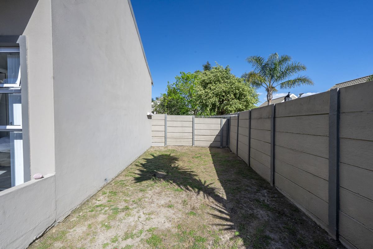 A side garden area featuring a precast concrete boundary wall and a patch of lawn adjacent to the main building structure.