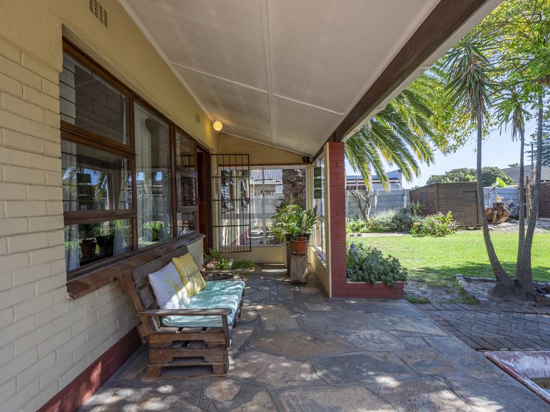 A covered patio area featuring stone paving, brick accents, and direct access to the rear garden, providing a functional outdoor living space.
