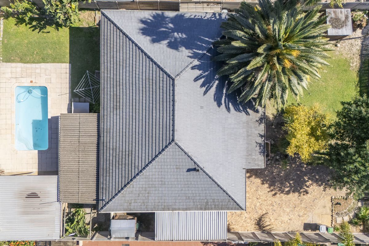Aerial view of the property showing the tiled roof, swimming pool, paved patio area, and surrounding garden space.