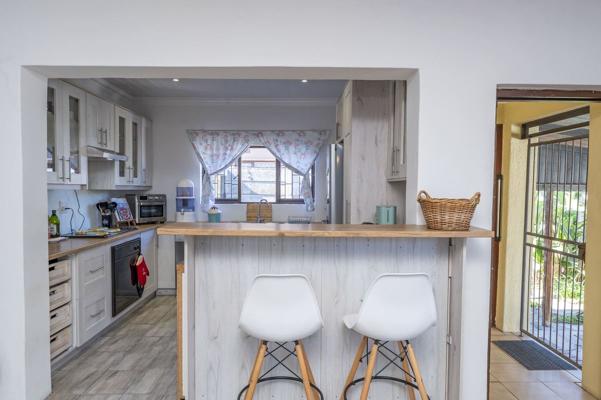 A functional kitchen featuring light-toned cabinetry, a built-in oven, extractor fan, and a breakfast bar counter overlooking the adjacent space.