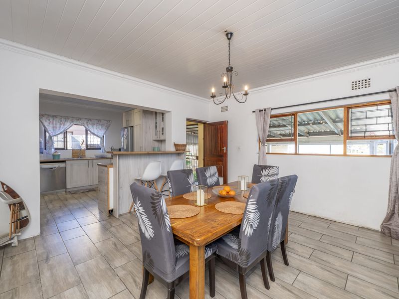 Open-plan dining area featuring timber-look tile flooring and a tongue and groove ceiling, seamlessly connected to a functional kitchen with a breakfast bar.