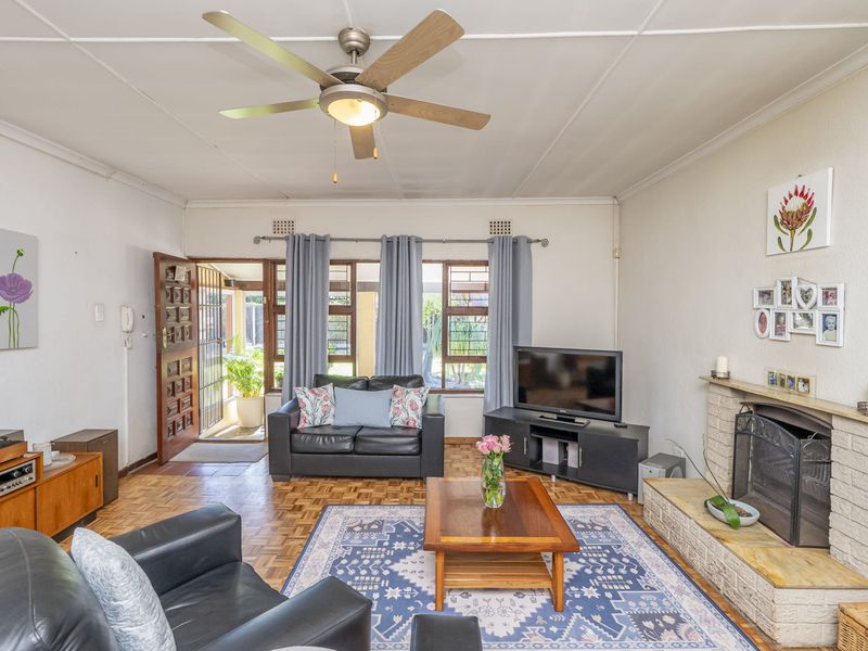 A living room featuring parquet flooring, a brick fireplace, and a ceiling fan, with direct access to the exterior through a timber door.