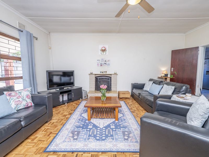 A comfortable living room featuring classic parquet flooring, a central brick fireplace, and a ceiling fan, offering a warm and functional living space.