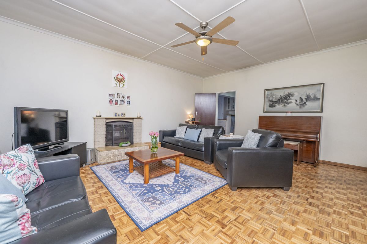 Spacious living room featuring classic parquet flooring, a brick fireplace, and a ceiling fan, offering a comfortable and traditional living space.