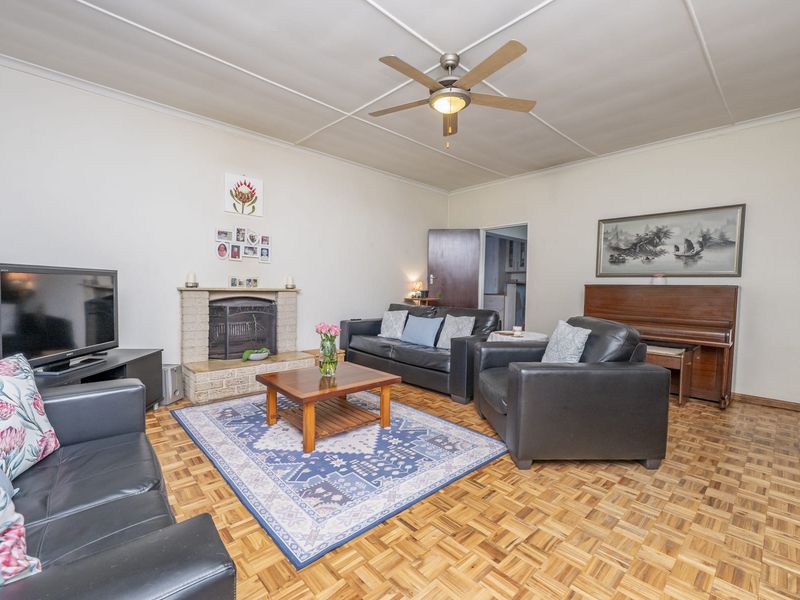 Spacious living room featuring classic parquet flooring, a brick fireplace, and a ceiling fan, offering a comfortable and traditional living space.