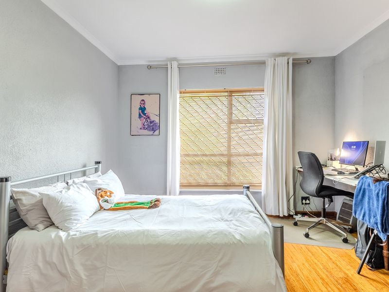 A functional bedroom featuring timber flooring, neutral wall tones, and a window fitted with venetian blinds, providing a comfortable living space.