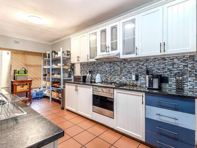 A functional kitchen featuring white and blue cabinetry, granite countertops, a mosaic tile backsplash, and integrated stainless steel appliances with tiled flooring.