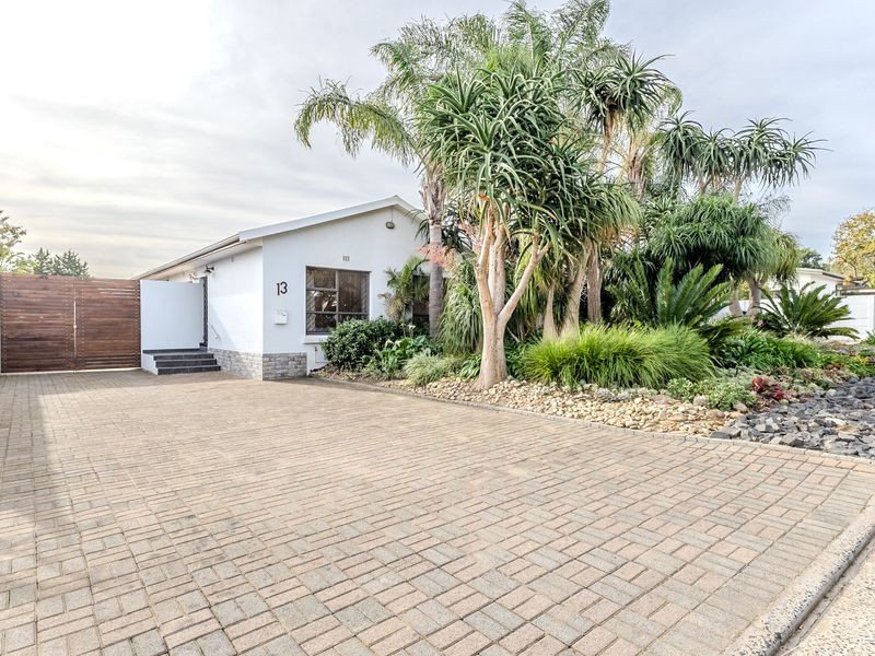 Front exterior view of the property featuring a paved driveway, landscaped garden, and secure timber gate entrance.