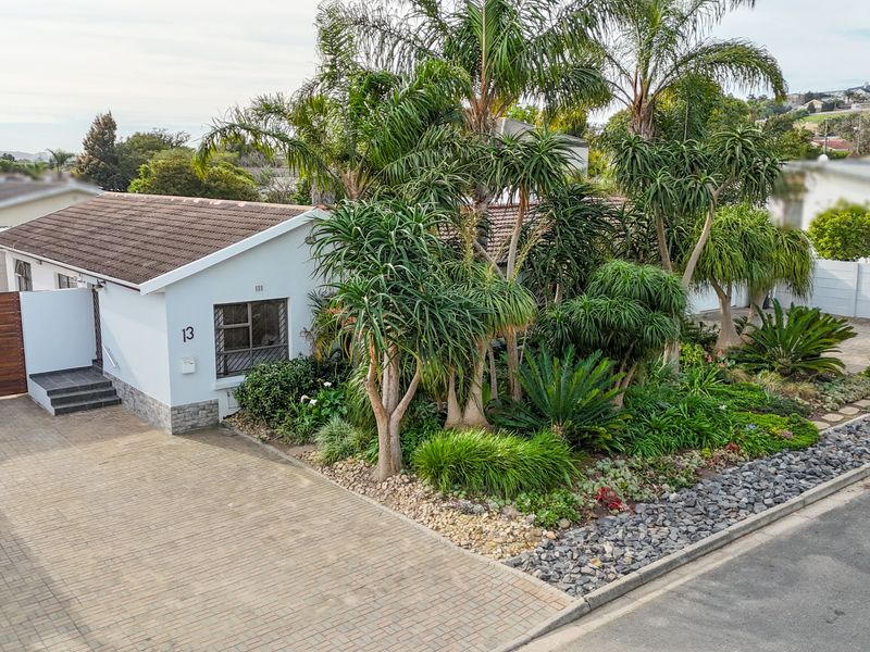 Front elevation of a well-maintained house featuring a paved driveway, timber gate, and established landscaped garden with mature trees.