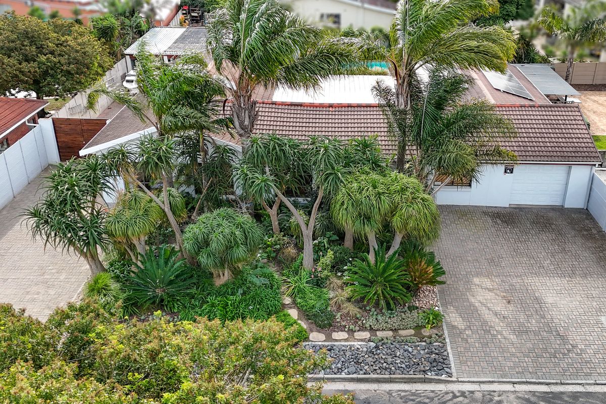 Aerial view of a residential property featuring a paved driveway, established garden with mature trees, tiled roof, and solar panels.