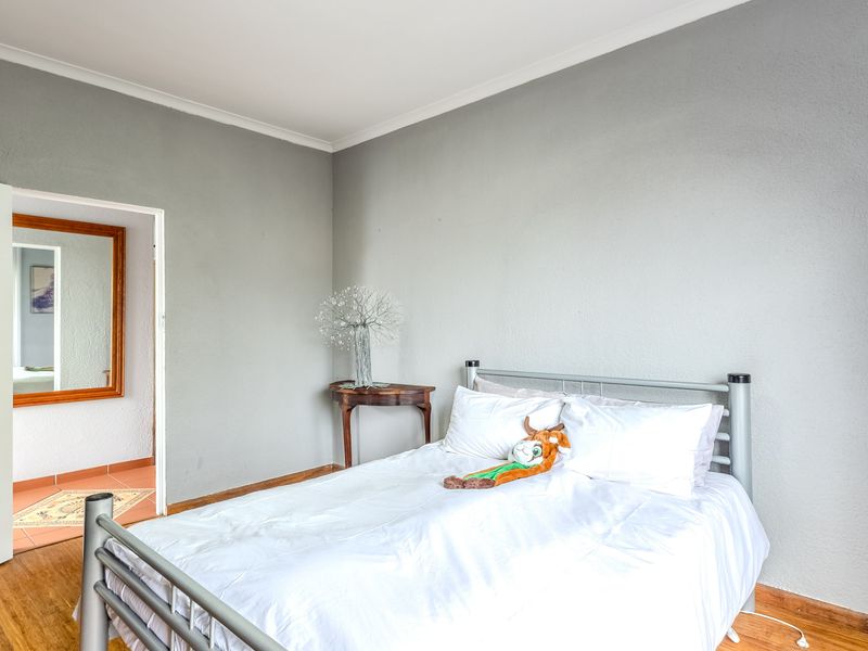 A bedroom featuring timber flooring and neutral grey walls, with an adjacent doorway leading to another room.
