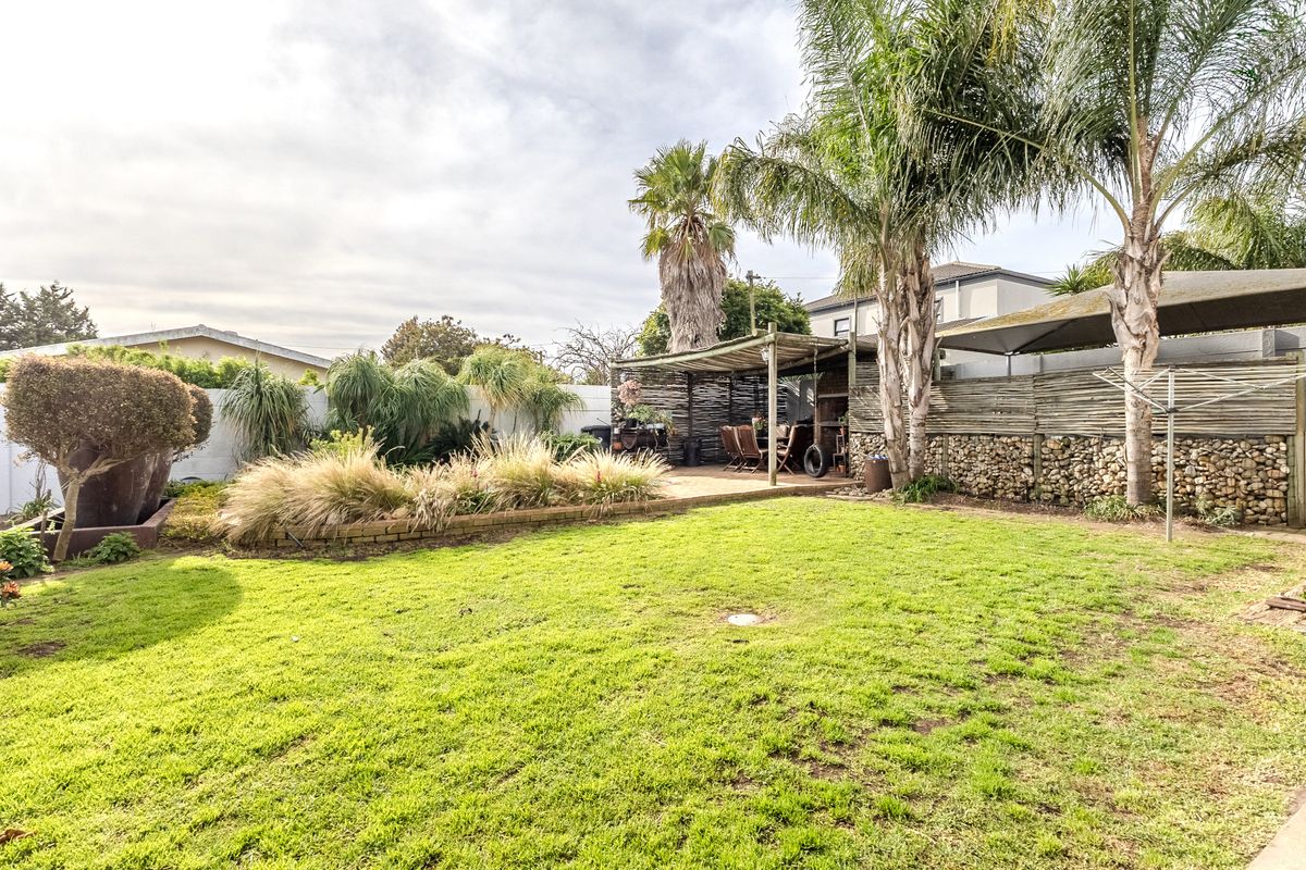 A spacious rear garden featuring a well-established lawn, mature palm trees, a stone retaining wall, and a timber pergola structure.