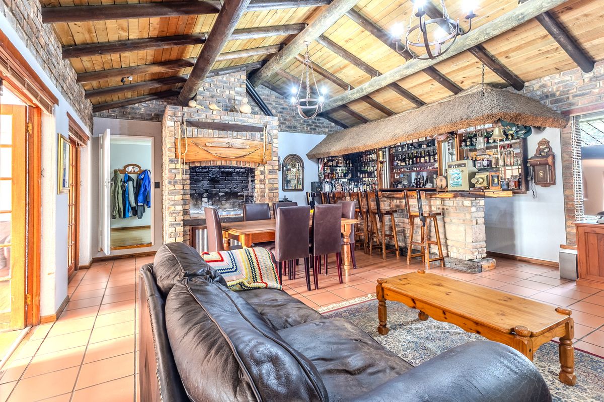 Spacious living area featuring a rustic brick fireplace, exposed timber beam ceiling, and a built-in bar with a unique thatched canopy.