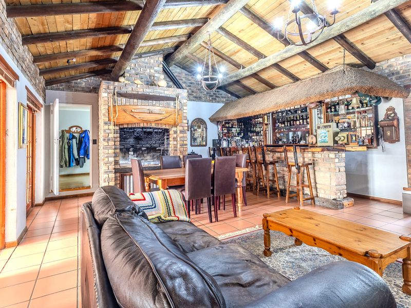 Spacious living area featuring a rustic brick fireplace, exposed timber beam ceiling, and a built-in bar with a unique thatched canopy.