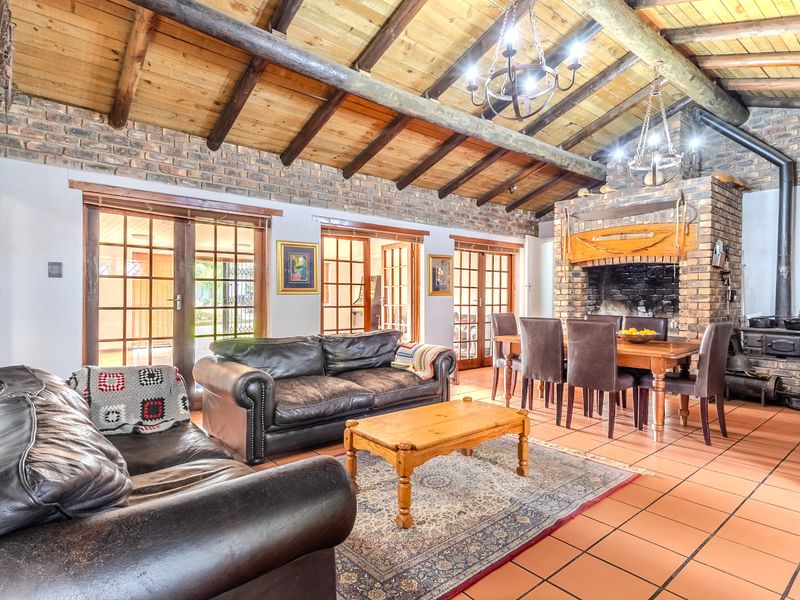 Spacious open-plan living and dining area featuring exposed timber beams, rustic brick walls, a large fireplace with a wood-burning stove, and terracotta flooring.