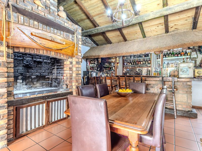 Rustic entertainment area featuring a large built-in brick fireplace, a fully equipped bar with counter, and exposed timber beam ceilings.