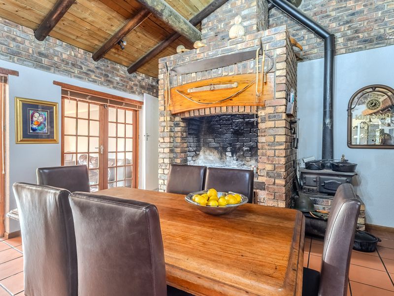 Dining room featuring a prominent exposed brick fireplace, wood-burning stove, exposed timber ceiling beams, and tiled flooring with access through french doors.