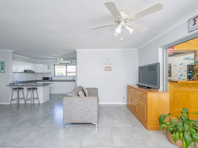 Open-plan living area featuring tiled flooring, a ceiling fan, and a functional kitchen with white cabinetry and a breakfast bar island.