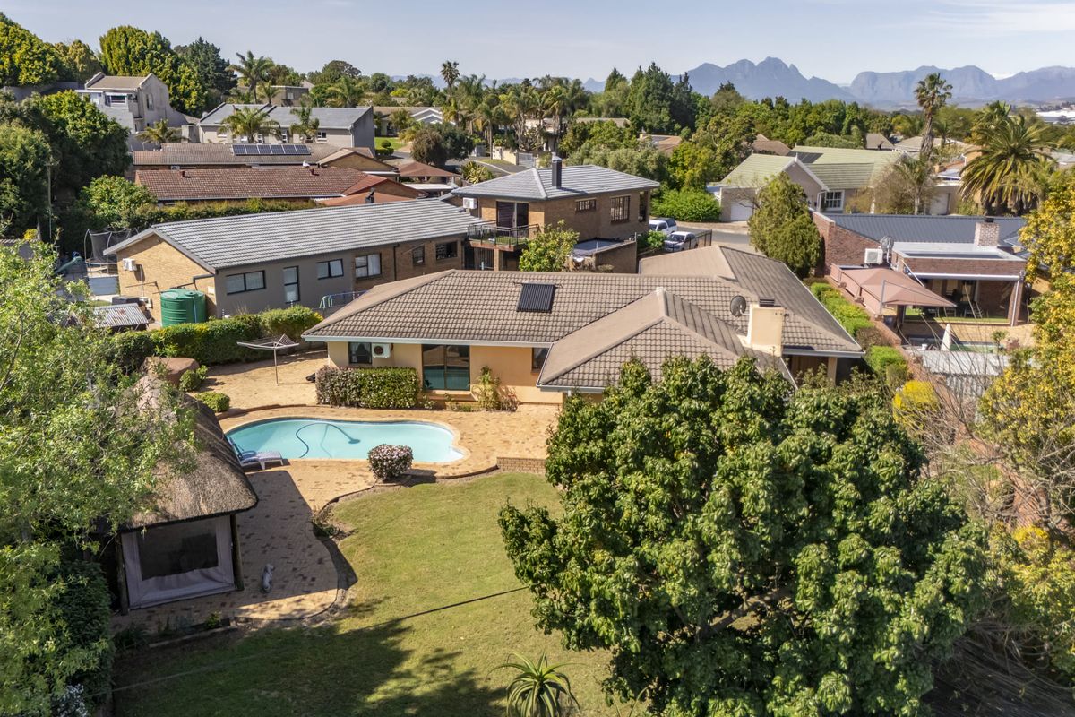 Aerial view of the property featuring a swimming pool, thatched lapa, paved patio, and established garden within a residential neighbourhood.