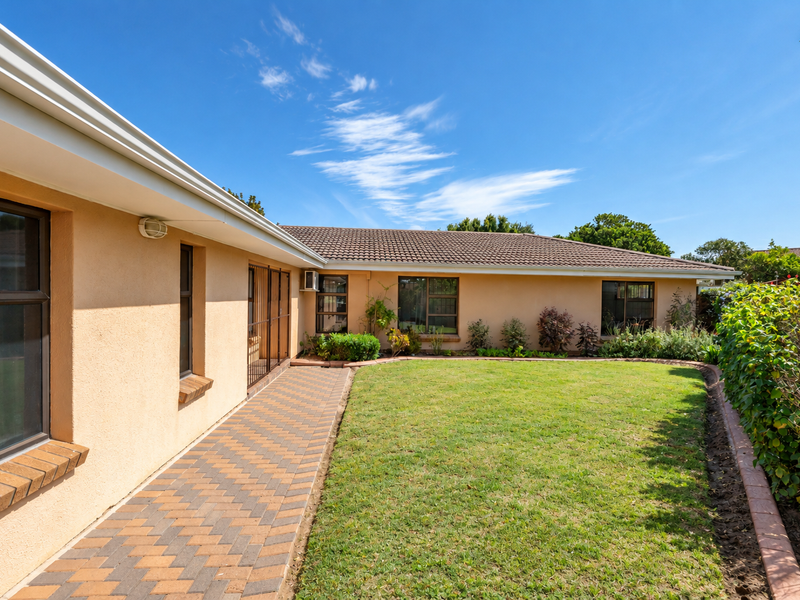 A well-maintained rear exterior view featuring a neat lawn, a brick-paved walkway, and established garden borders against the house facade.