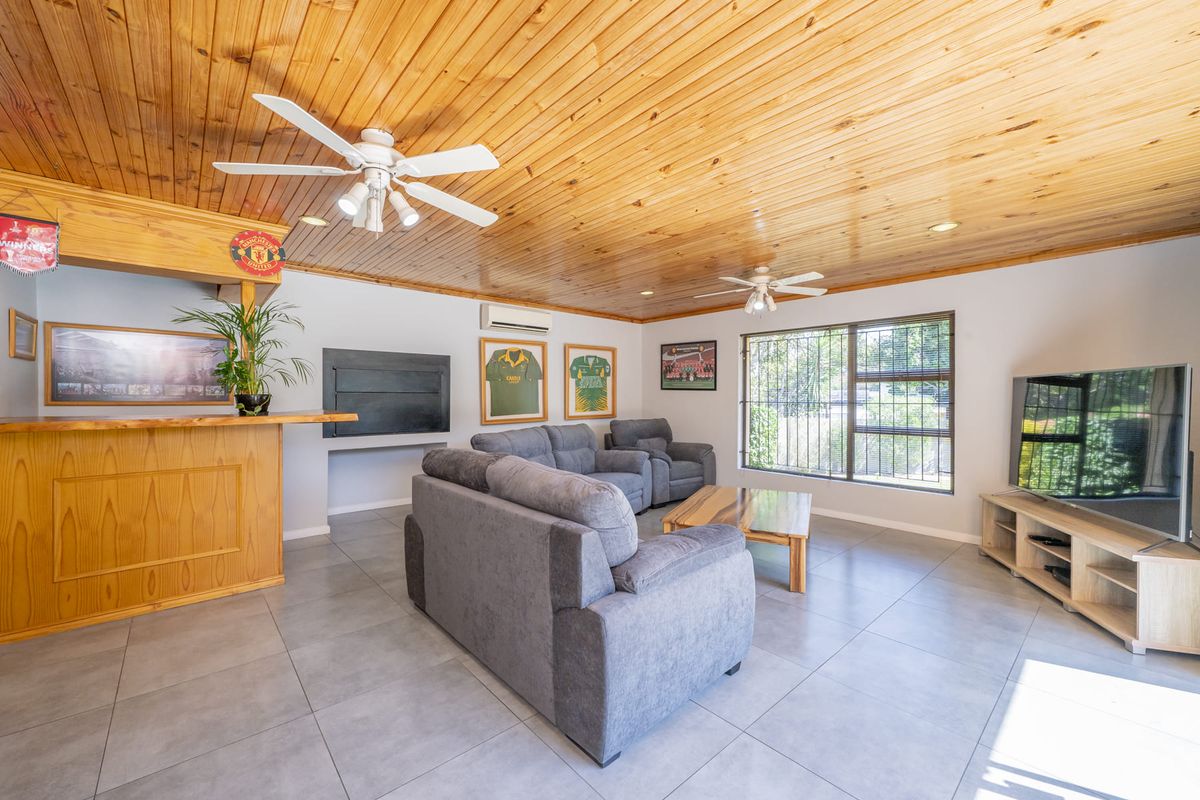 Spacious living room featuring a timber-clad ceiling, built-in bar, fireplace, and tiled flooring, offering a comfortable and functional entertainment space.
