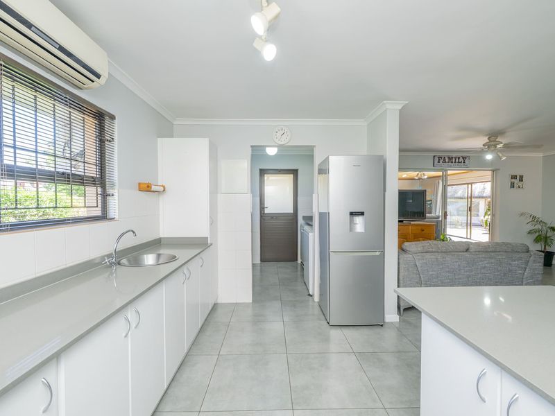 A clean, functional kitchen featuring white cabinetry, stone countertops, tiled flooring, and a split-system air conditioner, flowing into an adjacent living area.