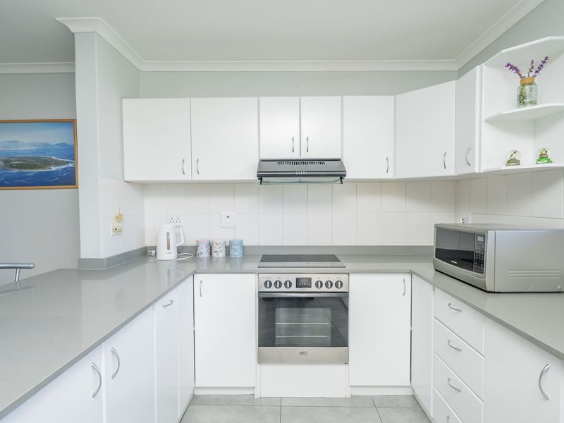 A clean and functional kitchen featuring white cabinetry, stone countertops, a built-in oven, electric hob, and a tiled backsplash.