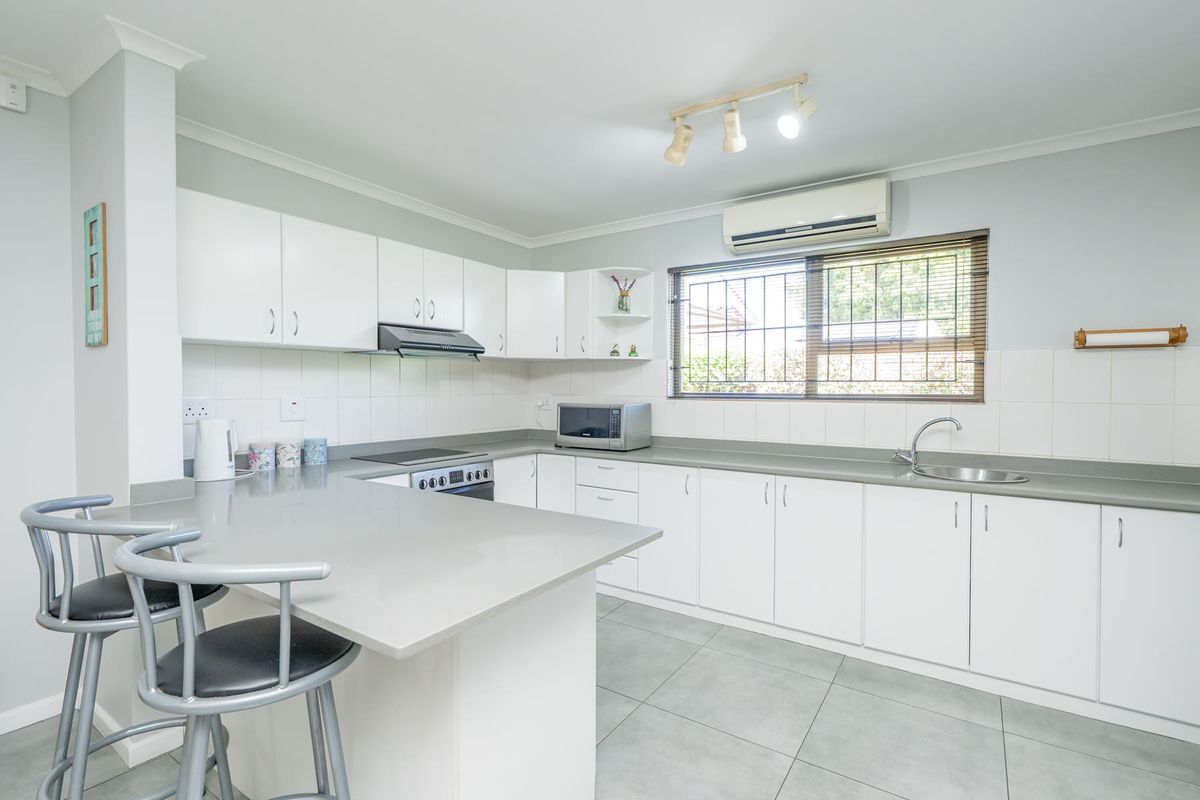 A clean, well-maintained kitchen featuring white cabinetry, stone countertops, integrated appliances, and tiled flooring with a breakfast bar area.
