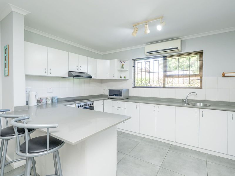 A clean, well-maintained kitchen featuring white cabinetry, stone countertops, integrated appliances, and tiled flooring with a breakfast bar area.