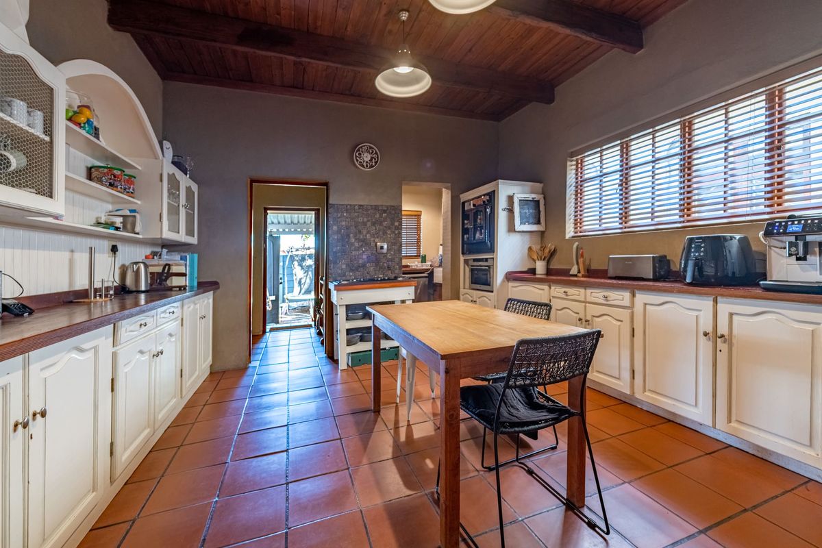 A rustic-style kitchen featuring timber ceilings, terracotta floor tiles, built-in cabinetry with timber countertops, and integrated appliances.