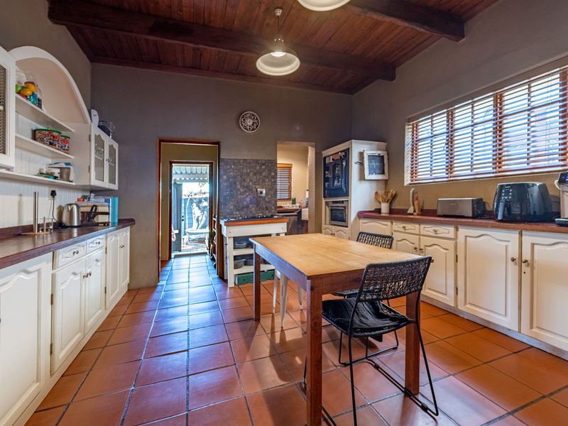 A rustic-style kitchen featuring timber ceilings, terracotta floor tiles, built-in cabinetry with timber countertops, and integrated appliances.