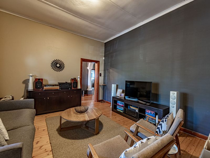 A living room featuring polished timber flooring, a coved ceiling, and a contrasting dark feature wall.