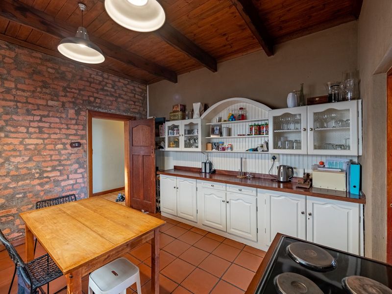 Rustic kitchen featuring exposed brick walls, timber beam ceilings, terracotta flooring, and classic white cabinetry with timber countertops.