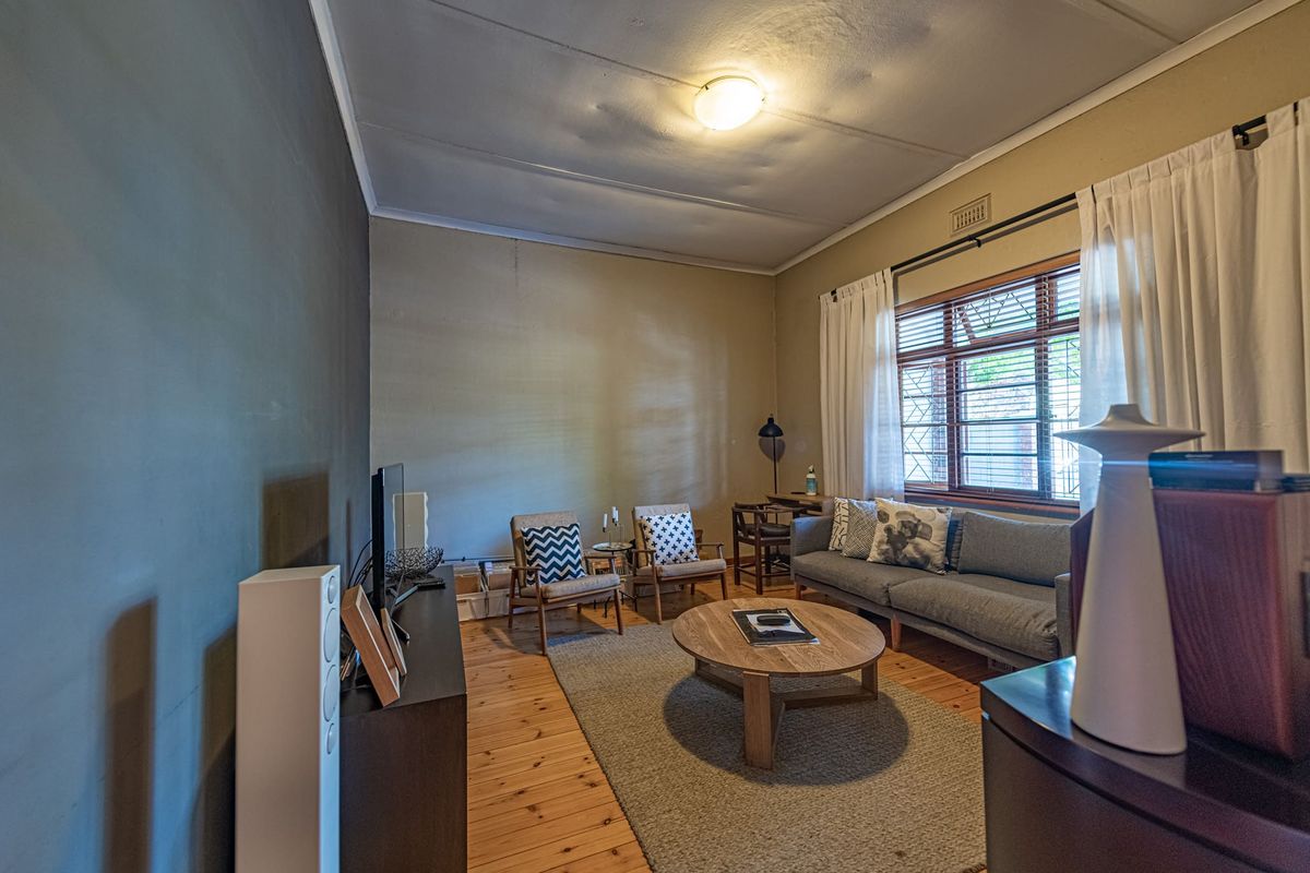 A cozy living room featuring warm timber flooring, a large window with security bars, and a central ceiling light fixture.