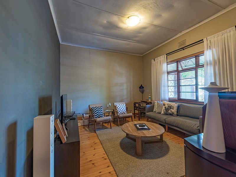 A cozy living room featuring warm timber flooring, a large window with security bars, and a central ceiling light fixture.
